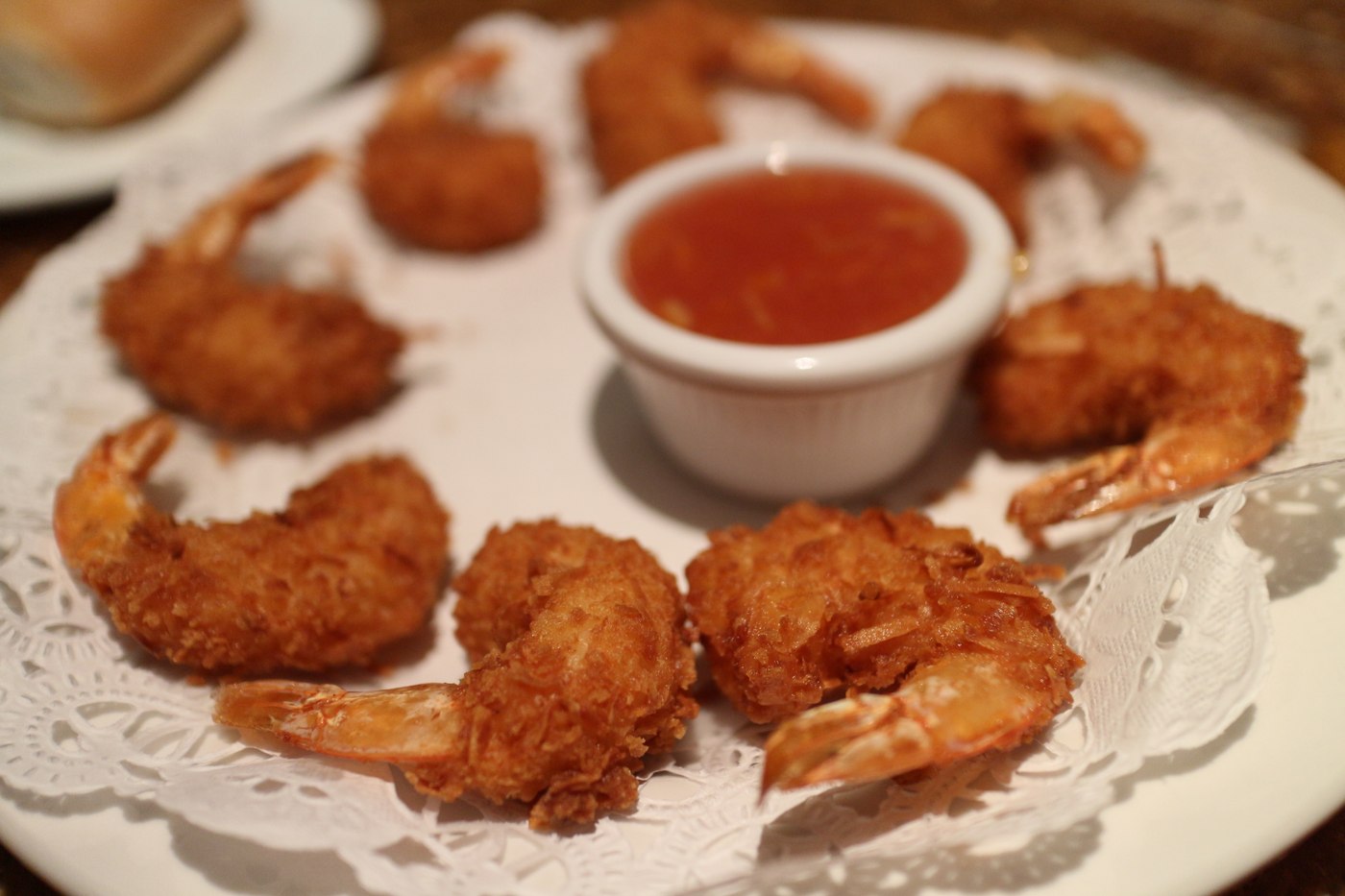 Golden coconut shrimp surround a small white cup of red dipping sauce on a white plate. Illustrative photo.