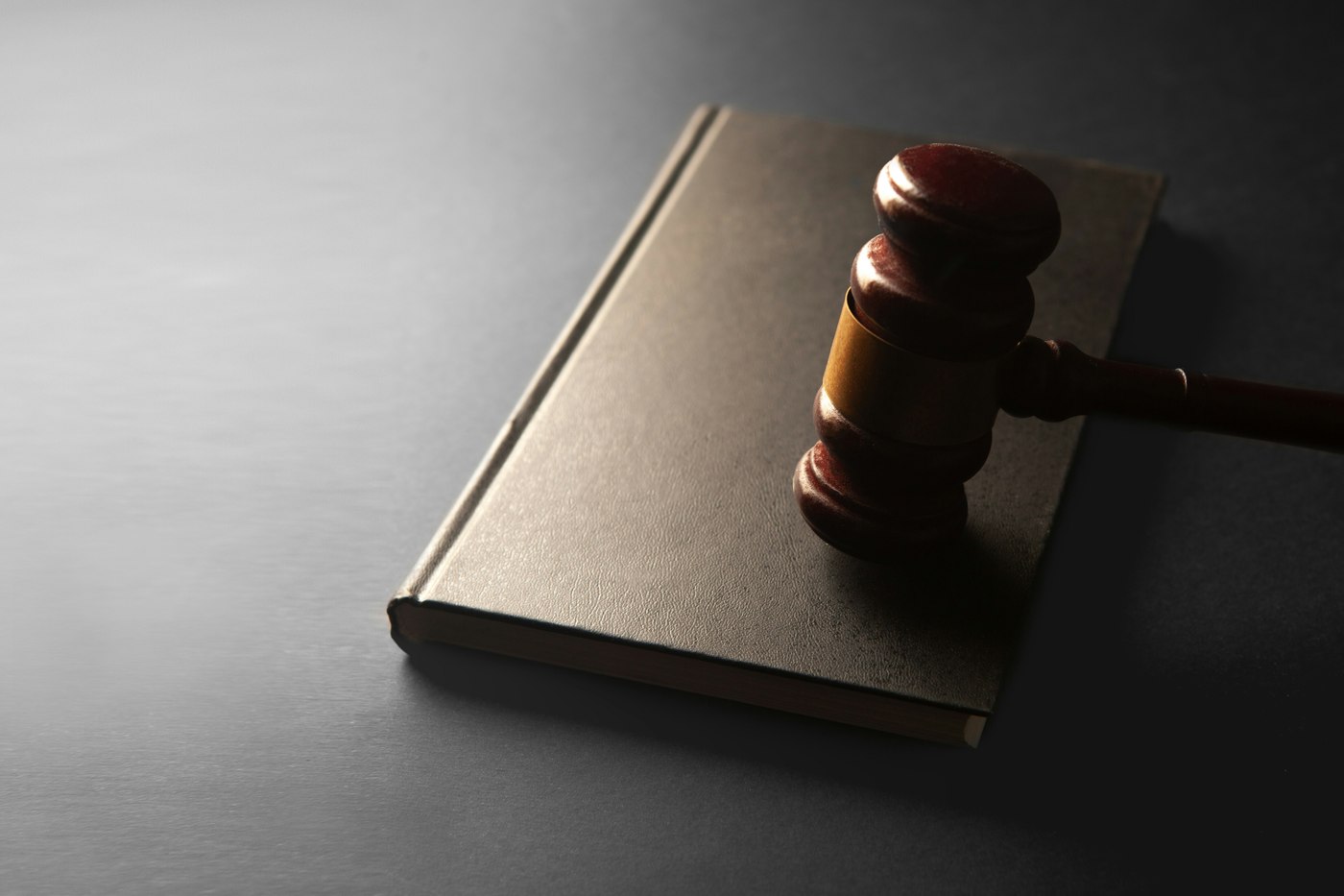 A wooden gavel rests on a closed, unmarked book on a dark tabletop. Illustrative photo.