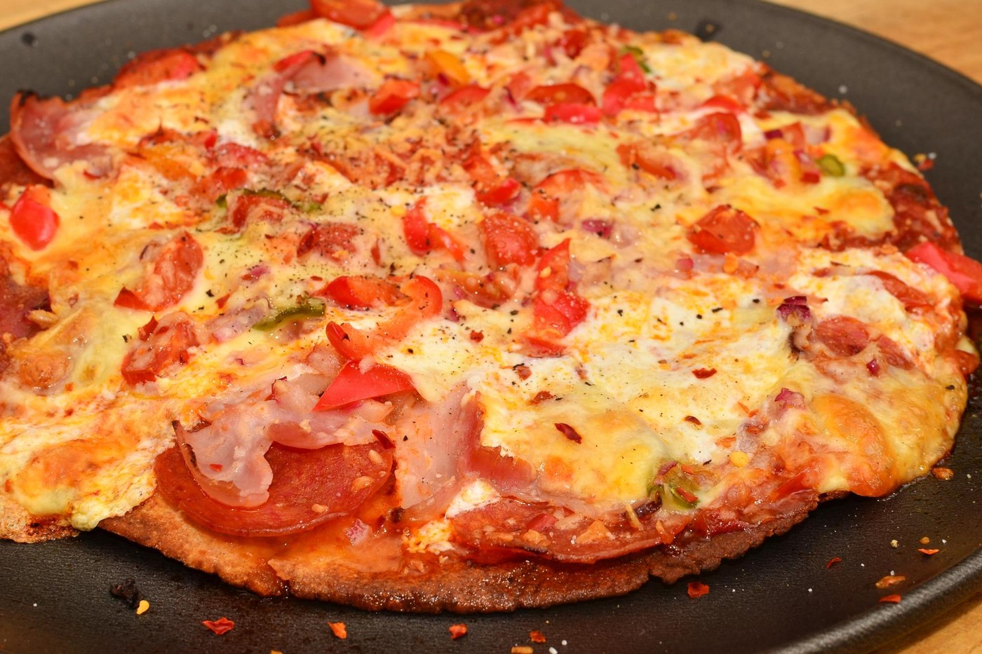 Closeup of homemade pizza with melted cheese, pepperoni, red peppers and onion on a dark baking tray. Illustrative photo.