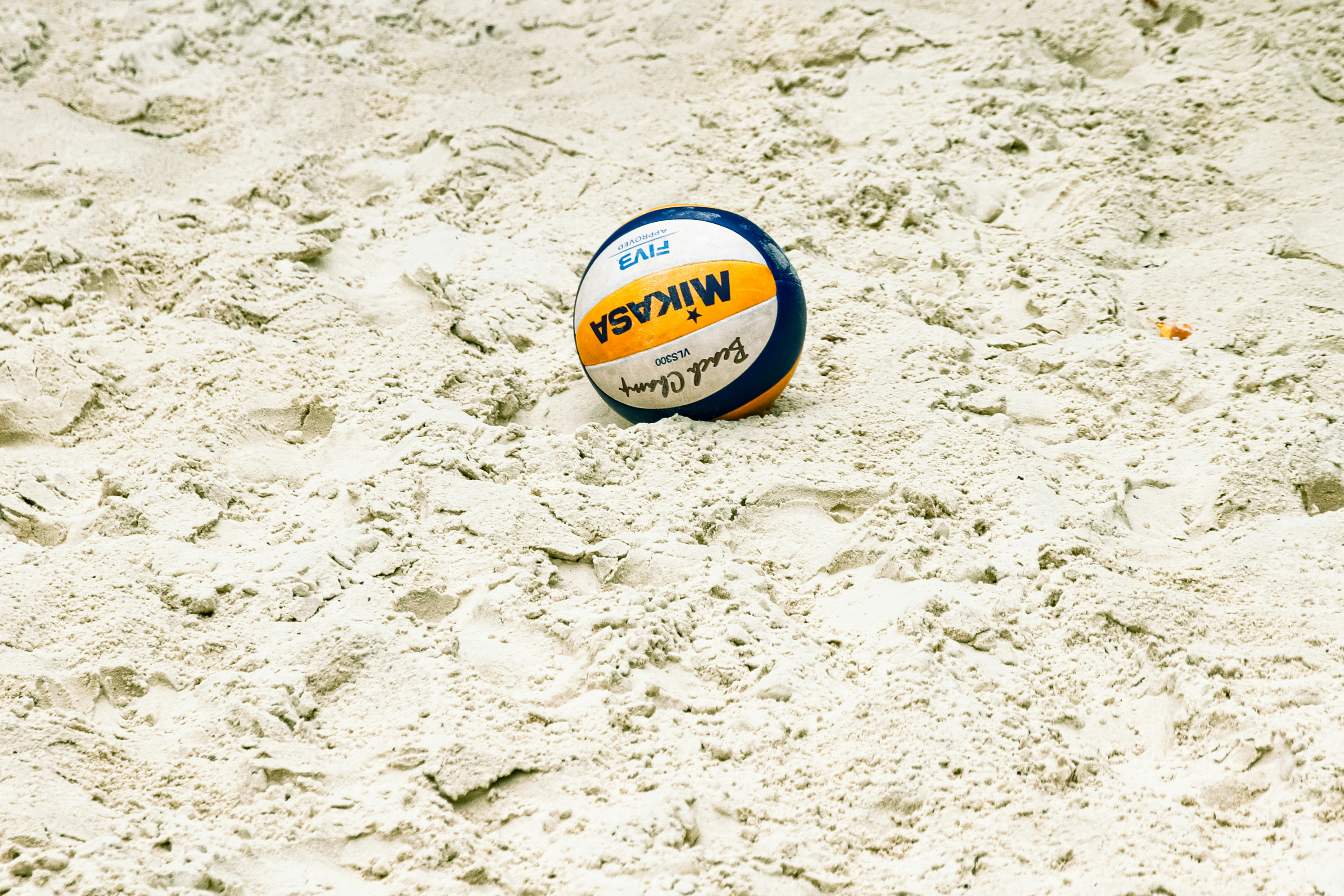 A yellow, blue and white volleyball rests on pale sand. Illustrative photo.