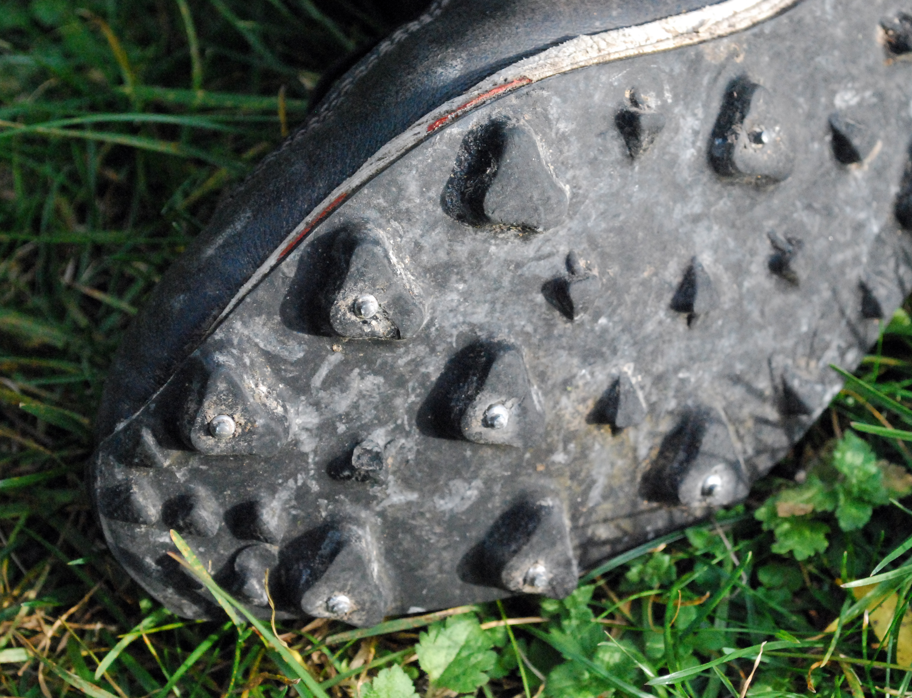 Closeup of a worn black studded shoe sole resting on grass. Illustrative photo.